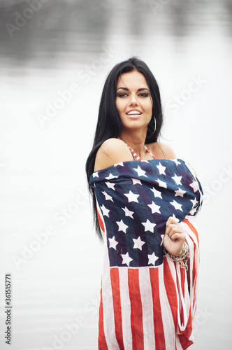 Smiling young beautiful woman with american flag on the beach