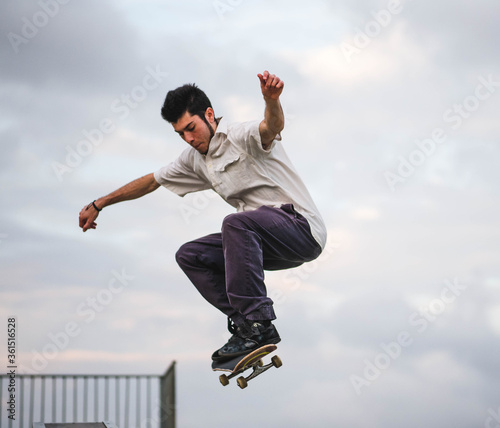 Young athletic male doing tricks with a skateboard at a skate park during daytime