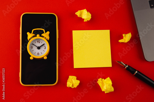 Home office workplace desk concept. Laptop, clock, smarpthone and sticky note on red background. photo