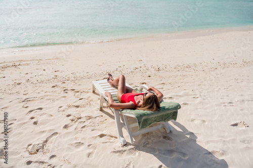 Full length photo of beautiful lady lying lounge chair azure blue water exotic resort empty desert beach sunbathing wear sun glasses red bodysuit enjoy sun rays ocean outside