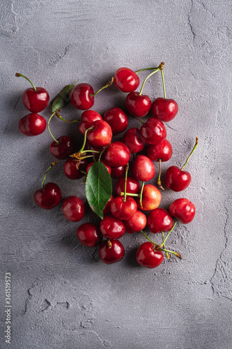 Fresh ripe cherry fruits with green leaves, summer vitamin berries on grey stone background, top view