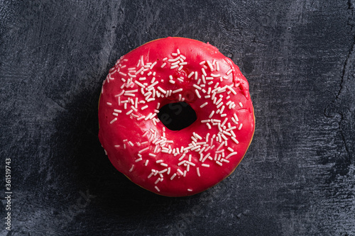 Pink donut with sprinkles, sweet glazed dessert food on dark concrete textured background, top view macro