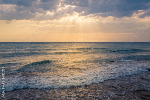 Calm sea waves hitting seashore. Beautiful summer day with sunrays shining through clouds. Endless horizon over the ocean