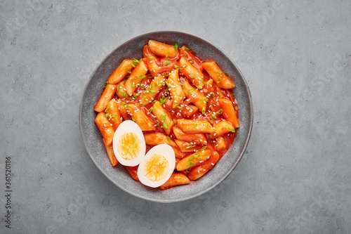 Tteokbokki with eggs in gray bowl on concrete table top. Tteok-bokki is a korean cuisine dish with rice cakes. Asian food. Top view photo