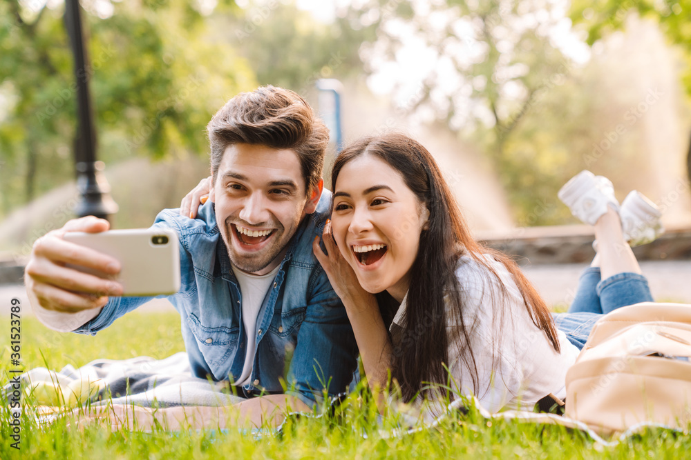 Image of happy couple taking selfie on smartphone while lying on grass Image of happy couple taking selfie on smartphone while lying on grass