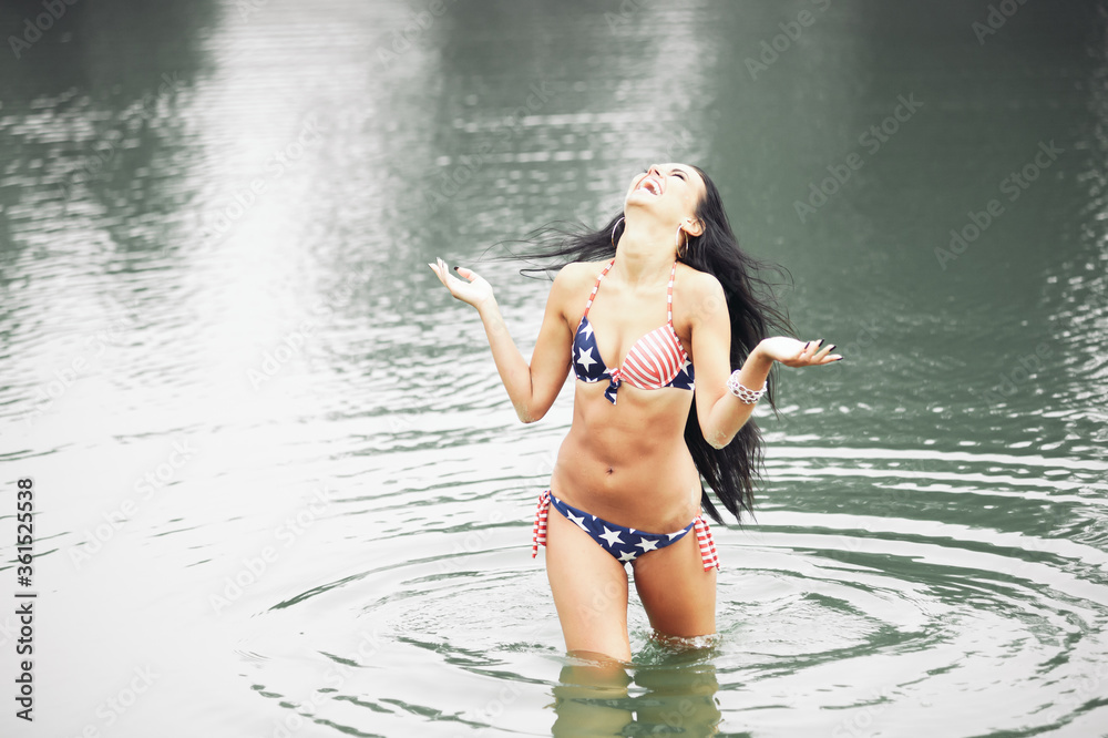 Woman on the beach in a swimsuit with an American flag having fun Woman on the beach in a swimsuit with an American flag having fun