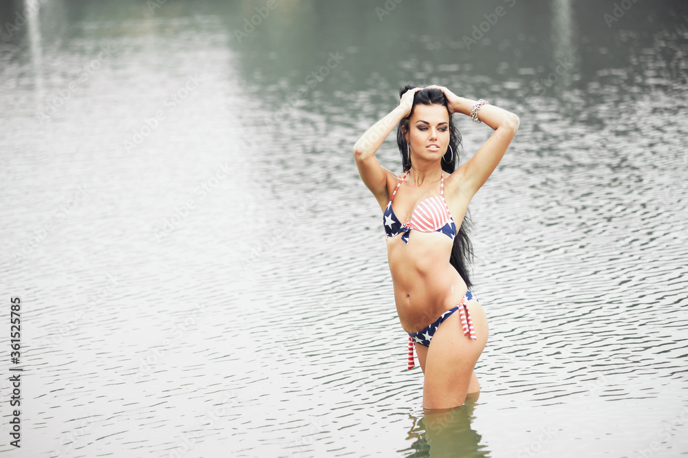 Woman on the beach in a bathing suit with an American flag having fun Woman on the beach in a bathing suit with an American flag having fun