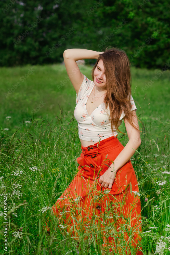 Soft focus of Young brunette girl in white top and red skirt standing in green meadow field grass in countryside looking a side touching her hair and enjoy nature and rural life Solo out door activity Soft focus of Young brunette girl in white top and red skirt standing in green meadow field grass in countryside looking a side touching her hair and enjoy nature and rural life Solo out door activity