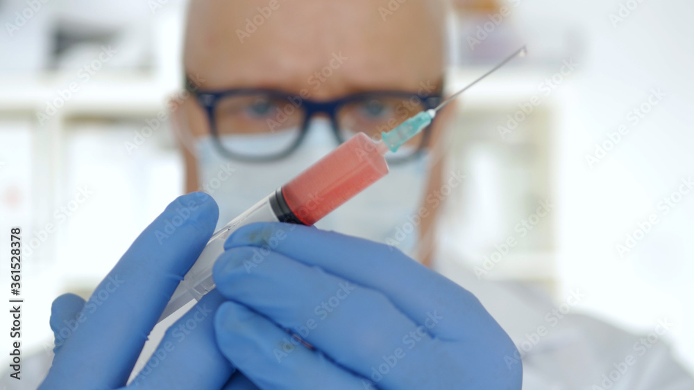 Doctor Wearing Protecting Gloves and Face Mask Keeping in His Hand an Injection with a Vaccine, Antidote, and Treatment for Covid-19 Virus Pandemic Doctor Wearing Protecting Gloves and Face Mask Keeping in His Hand an Injection with a Vaccine, Antidote, and Treatment for Covid-19 Virus Pandemic