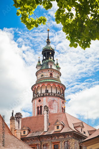 Tower of Cesky Krumlov state castle close up with lush tree branches in the foreground