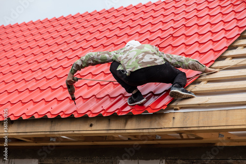 Workers install red metal tiles on the roof