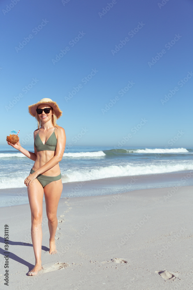 Woman with coconut cocktail walking on the beach
