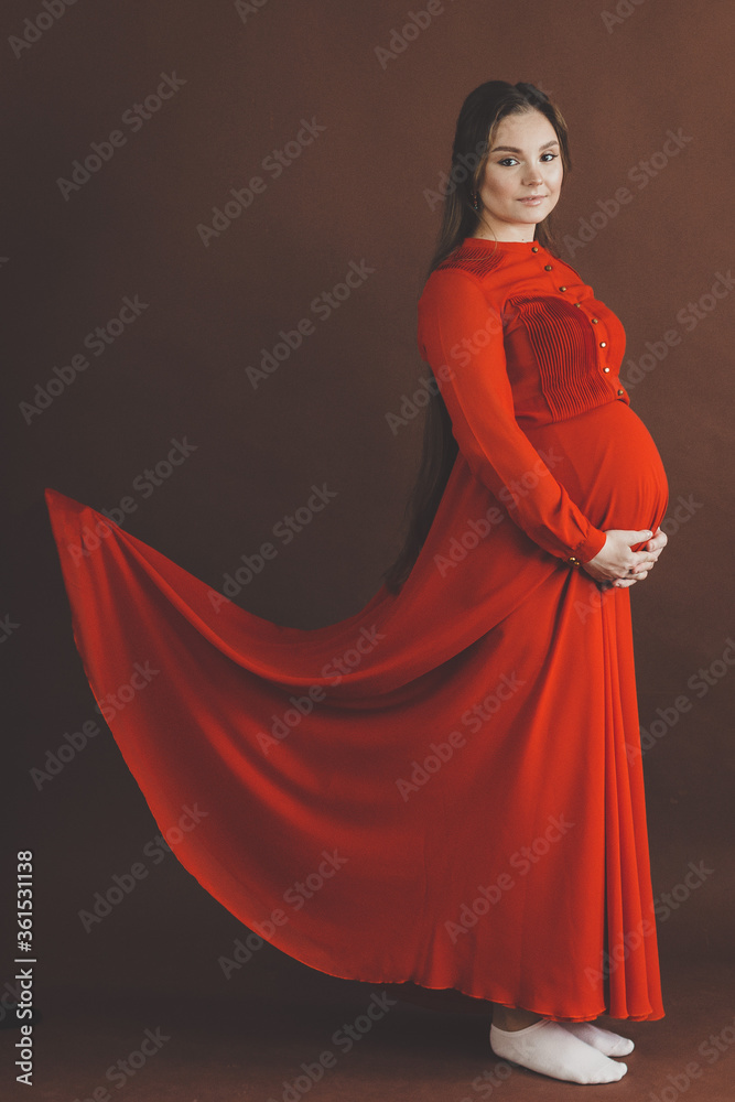 Naklejka premium Pregnant woman in red flying dress holding her belly.