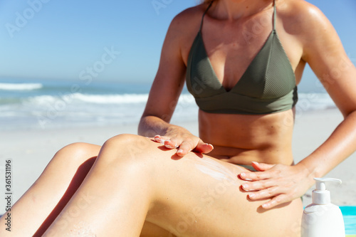 Mid section of woman applying sunscreen at the beach