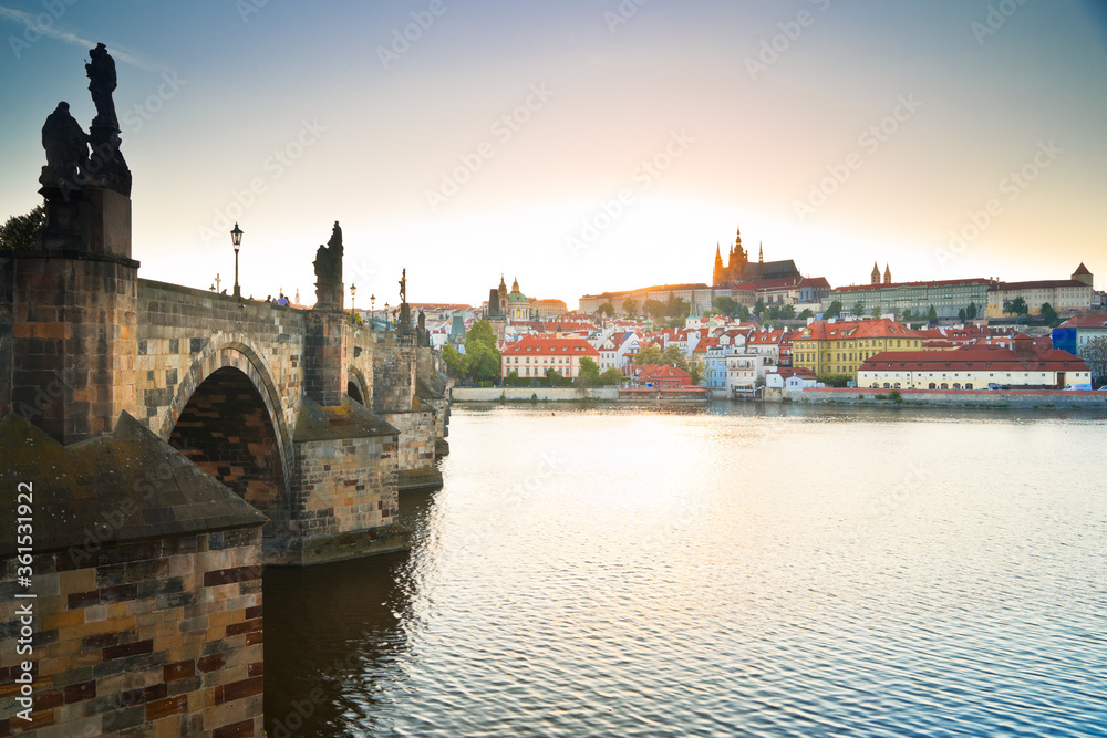 Side view of Charles bridge and Prague castle over the Vltava river with sun setting in the background