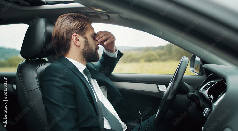 Tired businessman sitting on driver's seat touching bridge of nose staying somewhere in countryside Tired businessman sitting on driver's seat touching bridge of nose staying somewhere in countryside