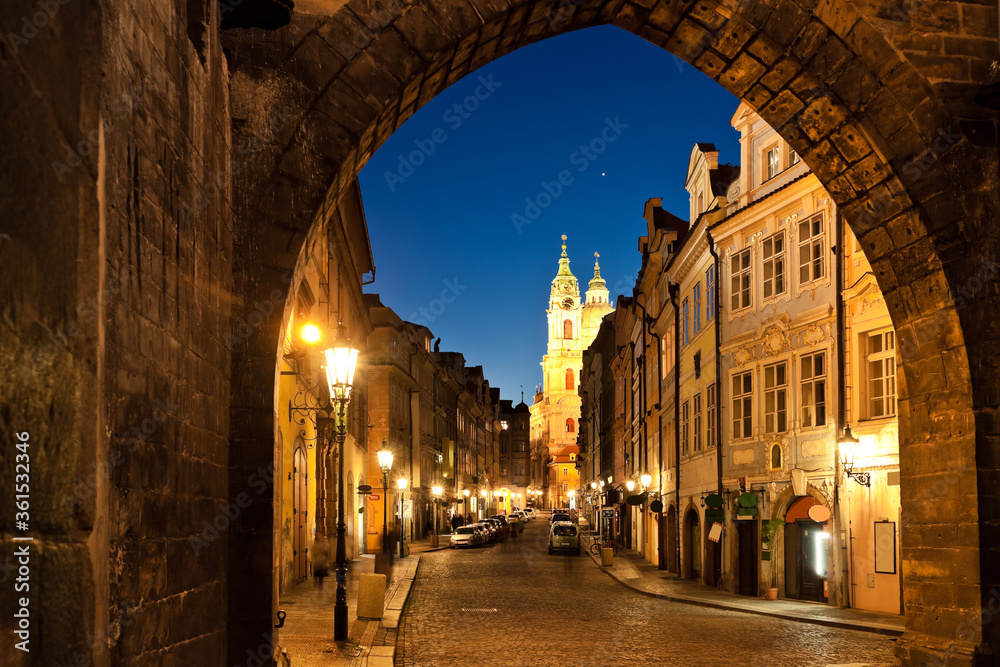 Framed view of a picturesque street leading to illuminated St. Nicholas church of Lesser town of Prague at twilight with no tourists during pandemic lockdown