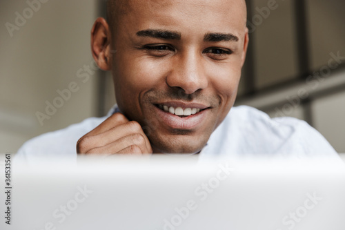 Photo of joyful african american man working with laptop and smiling