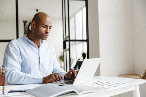 Photo of african american man working with laptop while sitting at table
