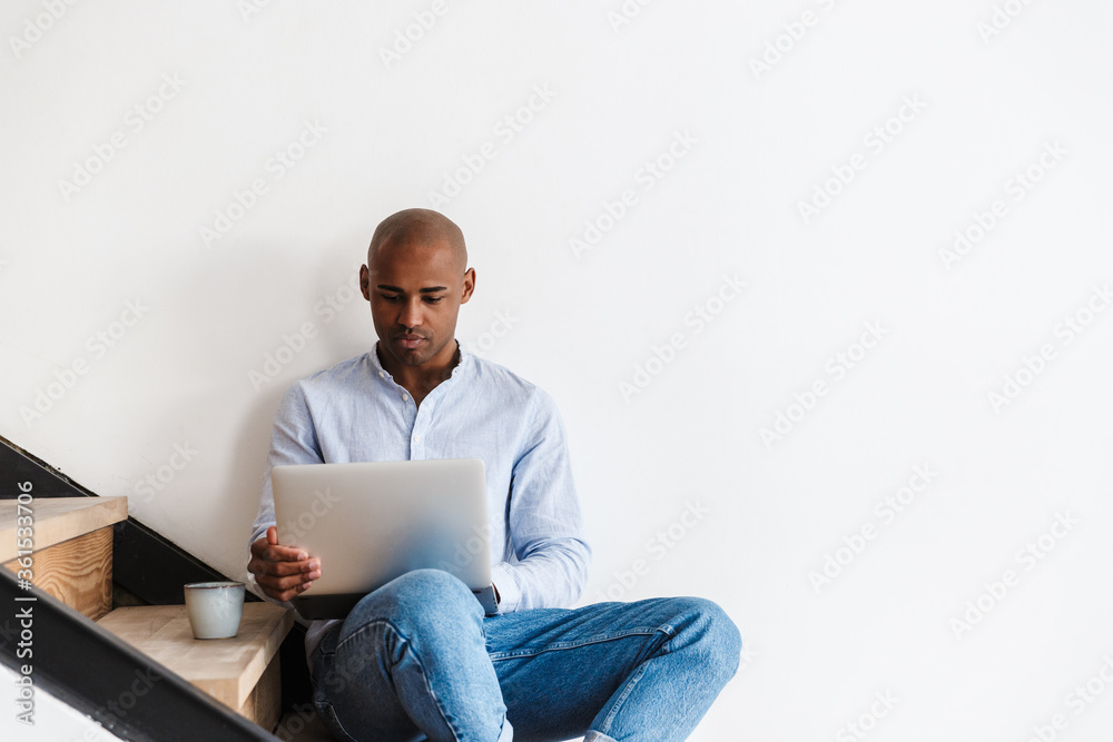 Photo of african american man working with laptop while sitting on stair