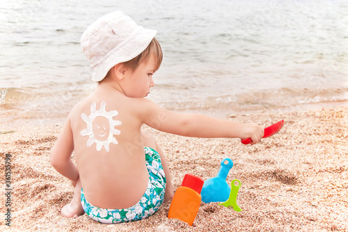 The sun drawing sunscreen on baby (boy) back. Beach.