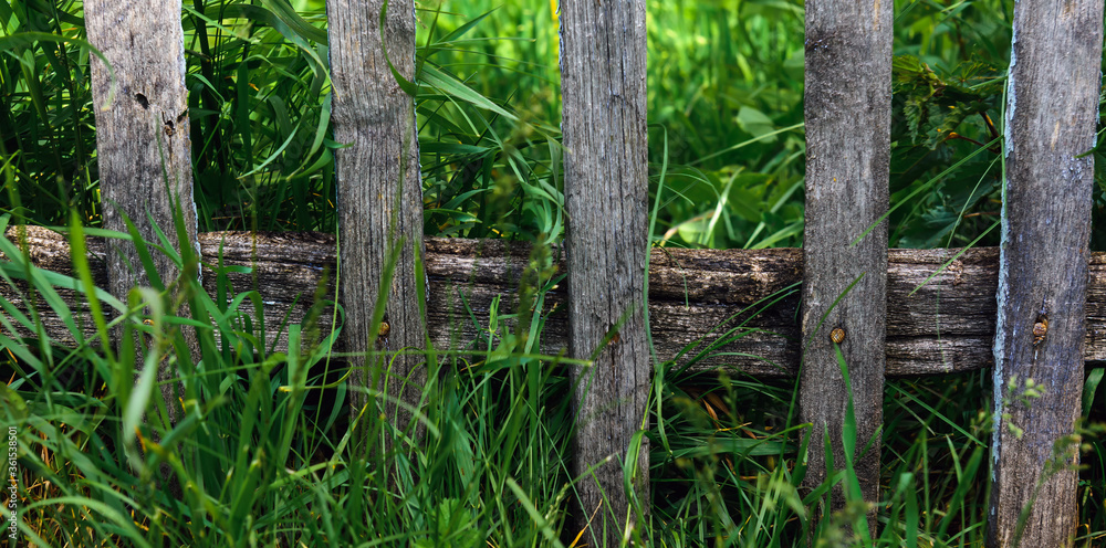 Old dilapidated wooden fence with rusty nails against of lush green grass. Concept of simple rural life. Village background. Old dilapidated wooden fence with rusty nails against of lush green grass. Concept of simple rural life. Village background.