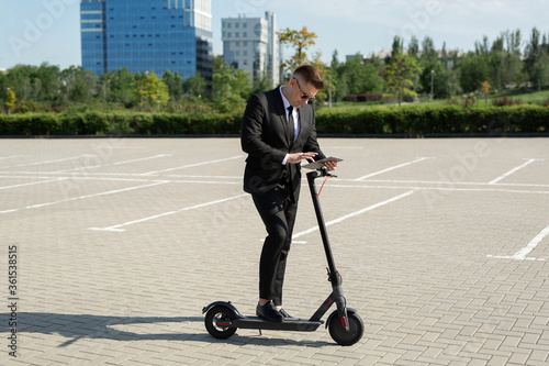 Young handsome businessman in a suit rides an electric scooter and looks at a laptop