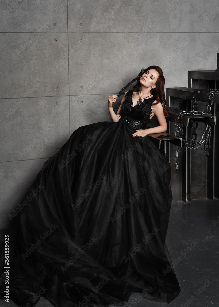Naklejka premium Young beautiful brunette woman standing in the palace room.Sexy girl.Halloween.Portrait of a girl in black.Beautiful woman in a darck room