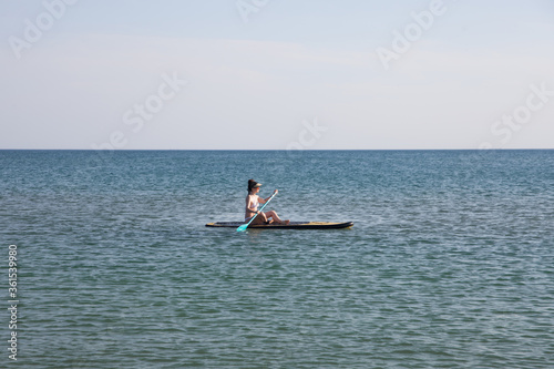 A young girl in a white swimsuit rides a sup Board. Healthy and active lifestyle.