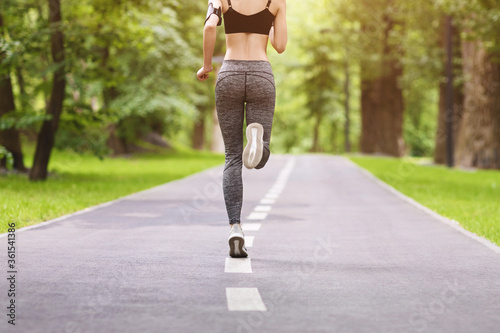 Unrecognizable Female Jogger Running On Path In Green City Park