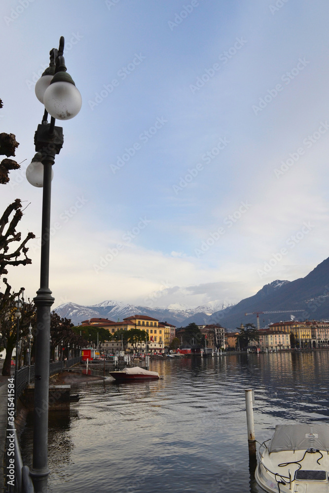 Landscape of the swiss city of Lugano. Street lamp (left), a fragment of the lake, boat. Alps in the fog in the background