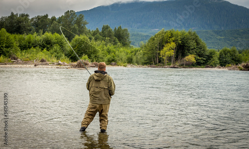 Fisherman battling a fish with a bent rod, while wading.