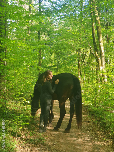 PORTRAIT: Happy woman smiles while wandering around forest with her horse.