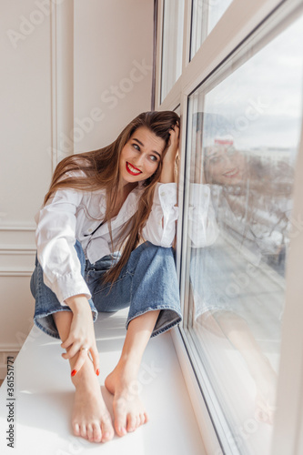 beautiful girl sitting on the window and smiling
