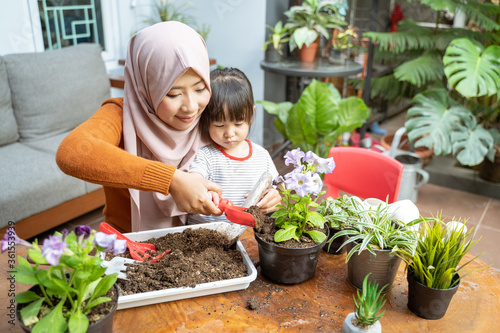 Asian mother helps her daughter hold a small shovel filled with soil to grow potted plants as a home activity © Odua Images