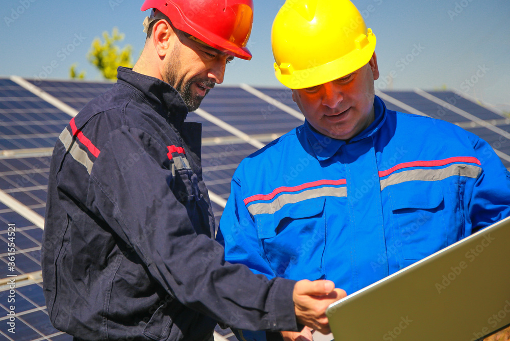 Green energy, power plant and two electricians with laptop Green energy, power plant and two electricians with laptop