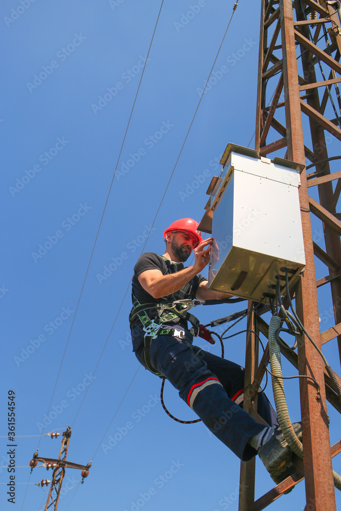 Electrician in red helmet working on power transmission line