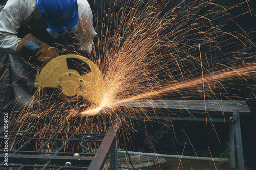Man wearing helmet, mask and glove using electric steel cutter machine working at workshop. Male cutting steel with sparks flying. Hard work factory or garage industry in construction site concept.