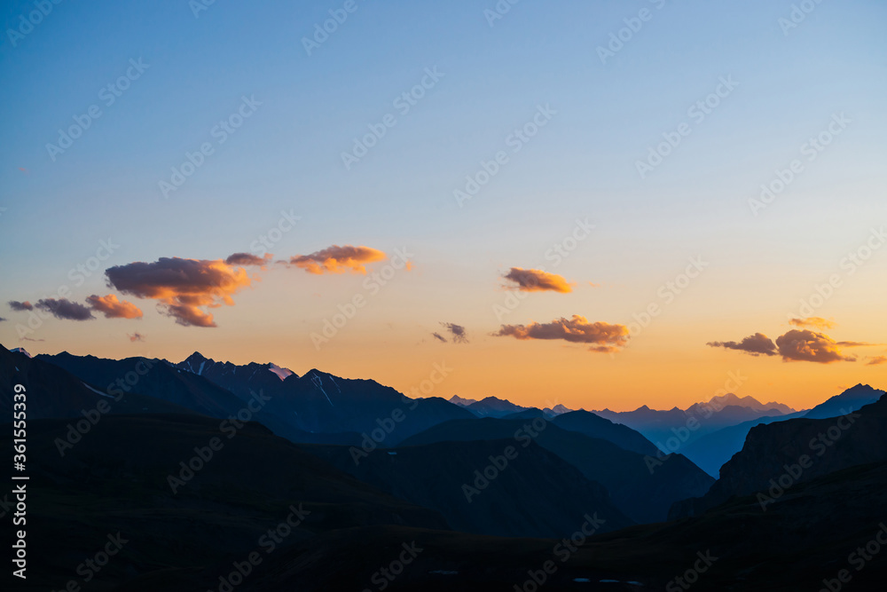 Colorful dawn landscape with beautiful mountains silhouettes and golden blue gradient sky with clouds. Vivid mountain scenery with picturesque multicolor sunset. Scenic sunrise view to mountain range. Colorful dawn landscape with beautiful mountains silhouettes and golden blue gradient sky with clouds. Vivid mountain scenery with picturesque multicolor sunset. Scenic sunrise view to mountain range.