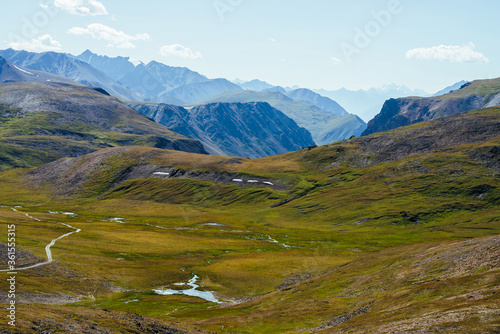Great rocky mountains and deep gorge behind beautiful green valley with lake in highlands. Awesome mountain landscape with giant rockies and deep abyss. Wonderful scenery with big rocks and precipice.