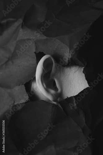 Woman's ear in hole in black crumpled paper background, black and white concept photography for blog or poster photo