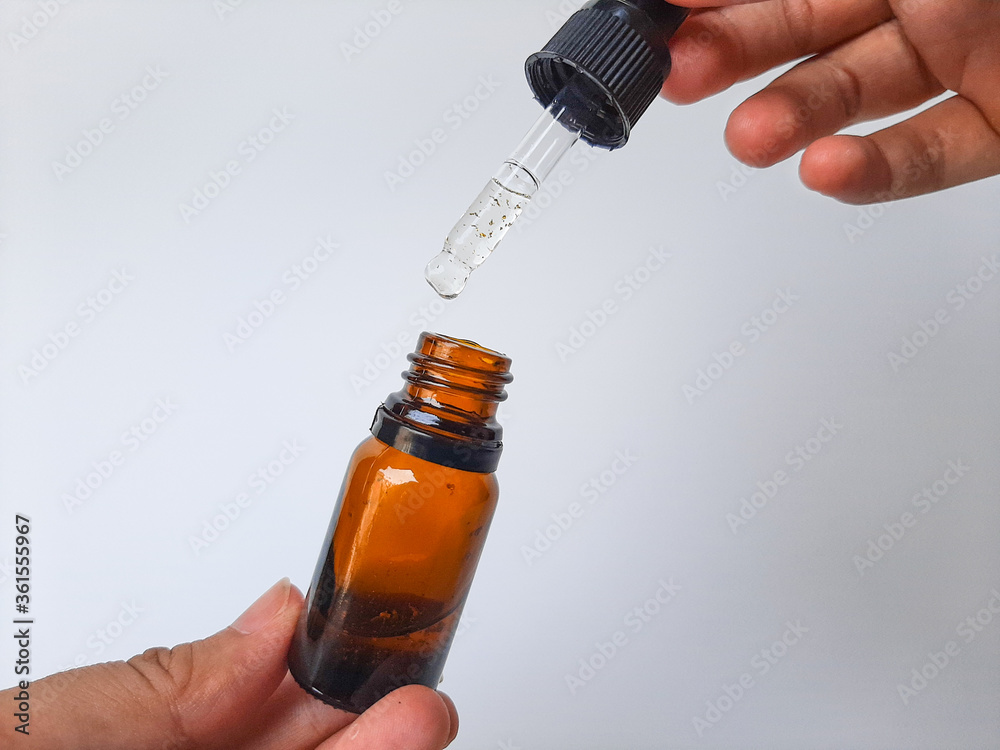 A hand holding a small glass pipette or dropper, that contain serum or skin care. Isolated in white background. A hand holding a small glass pipette or dropper, that contain serum or skin care. Isolated in white background.
