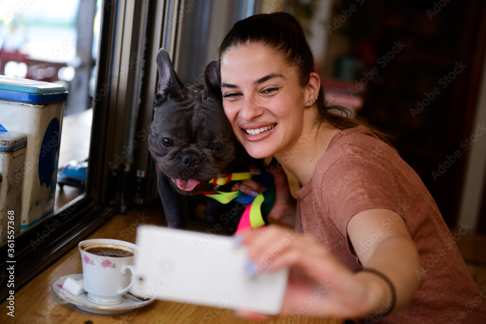 Young girl enjoying her free time with her adorable Blue French Bulldog and taking selfies inside a small, cosy, rustic pet friendly cafe. Young girl enjoying her free time with her adorable Blue French Bulldog and taking selfies inside a small, cosy, rustic pet friendly cafe.