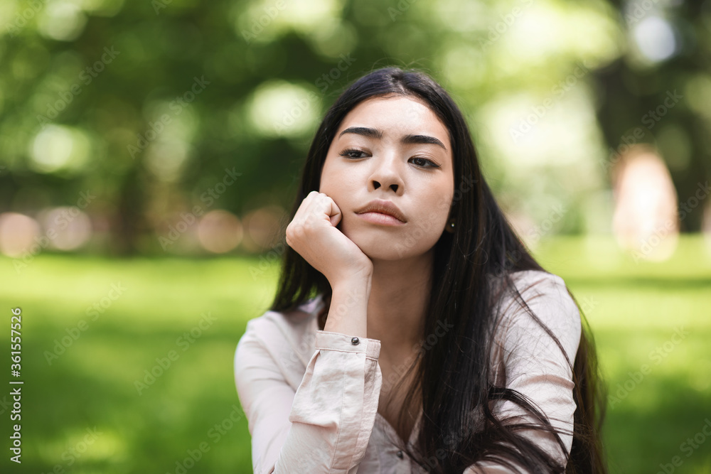 Pensive Asian Girl Sitting On Lawn In Park And Looking Away, Closeup Pensive Asian Girl Sitting On Lawn In Park And Looking Away, Closeup