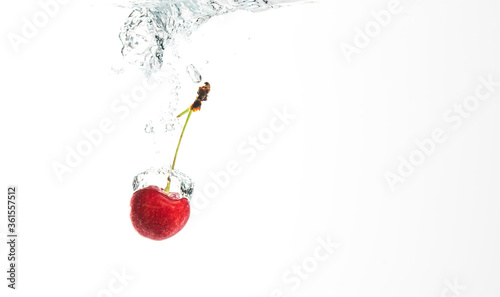 One red cherry splashing into crystal clear water with air bubbles.