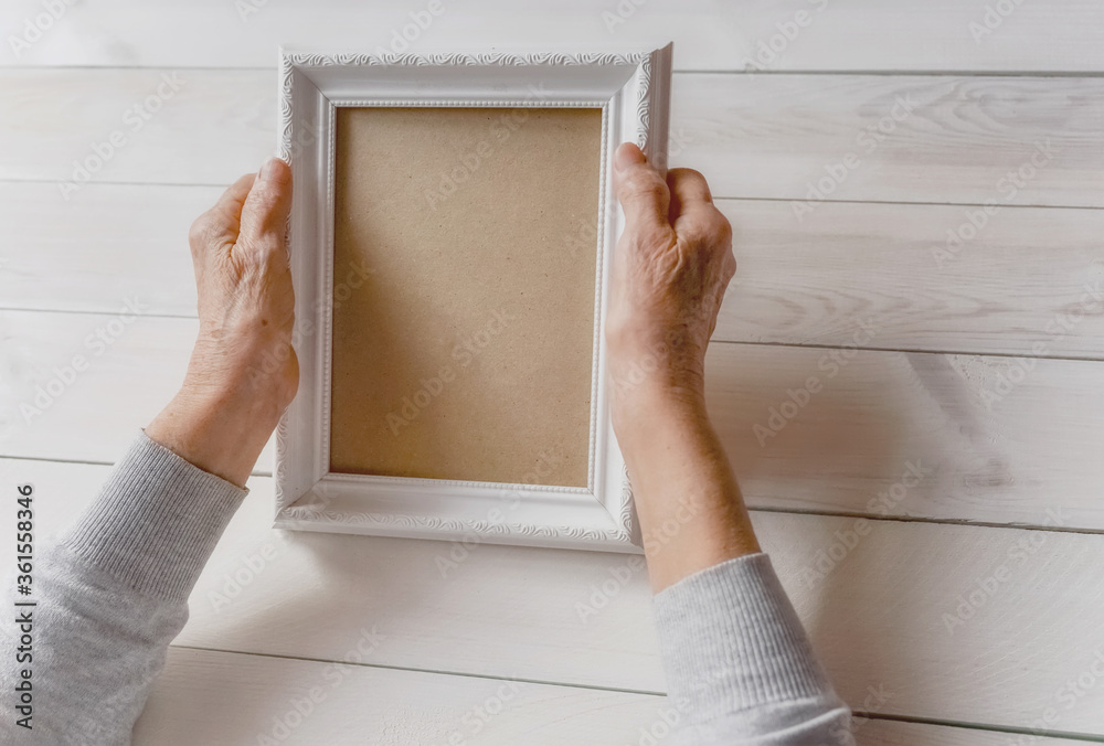 Senior wrinkled hands holding white photo frame. Elderly woman looking