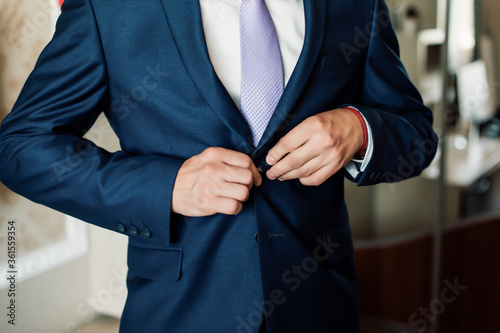 The groom is going to a dump in a suit and watch a tie with his hands