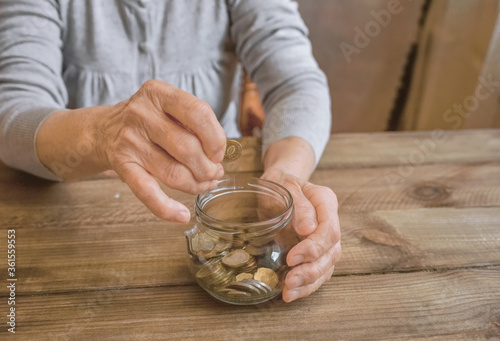 Old wrinkled hands holding jar with coins, wooden background. Elderly woman throws a coin into a jar, counting money. Saving money for future plan and retirement fund, pension, poorness, need concept.