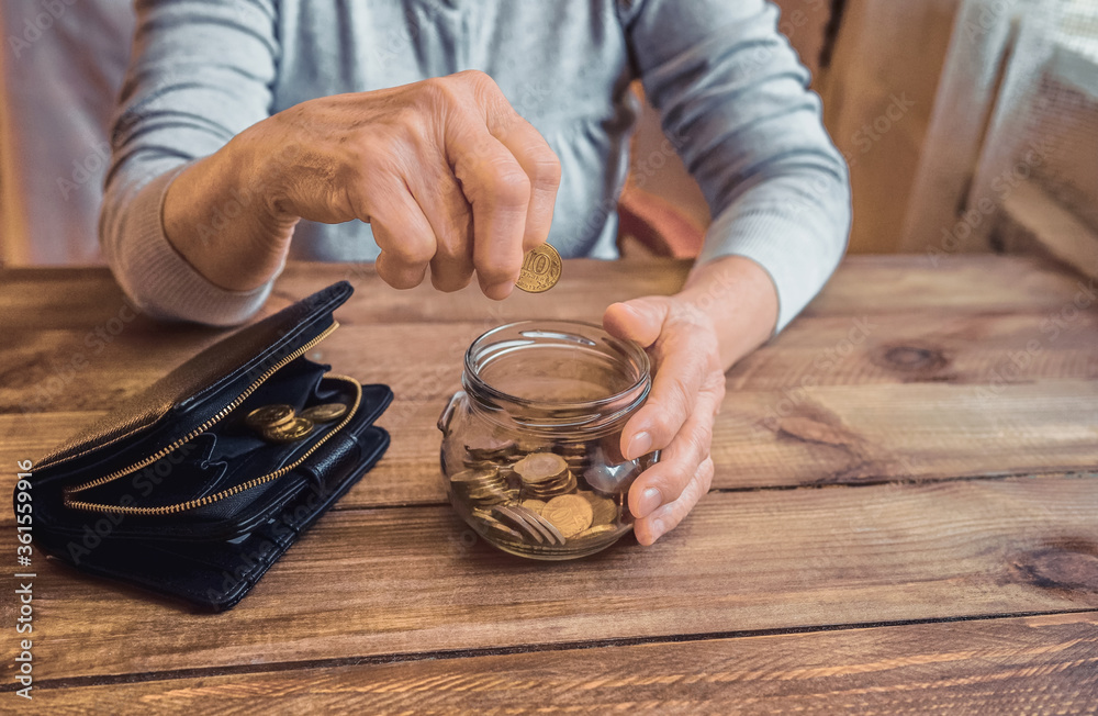 Old wrinkled hand holding jar with coins, empty wallet, wooden background. Elderly woman throws a coin into a jar, counting. Saving money for future, retirement fund, pension, poorness, need concept. Old wrinkled hand holding jar with coins, empty wallet, wooden background. Elderly woman throws a coin into a jar, counting. Saving money for future, retirement fund, pension, poorness, need concept.
