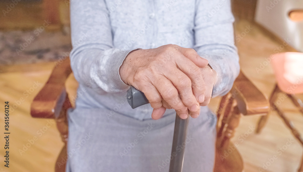 Old wrinkled hands on walking stick. Hands of a sitting senior woman holding a cane. Pension, care, poorness, need concept.